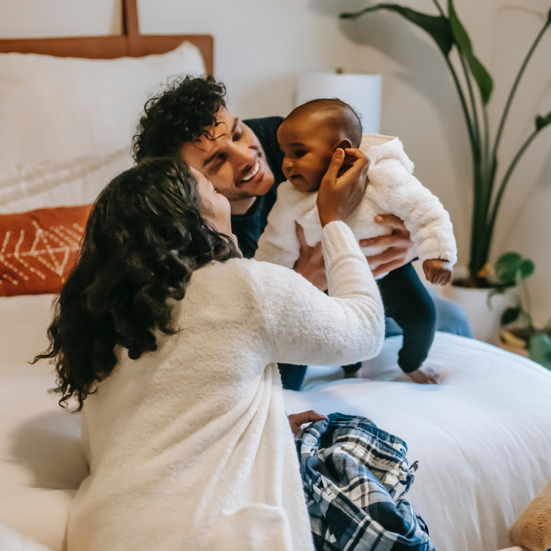 Parents play with newborn on bed