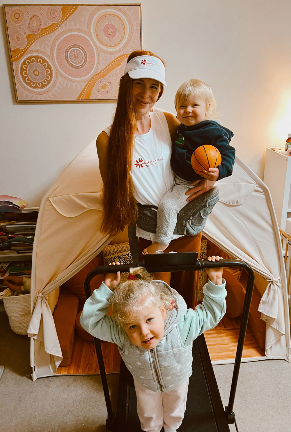 Mother holds two young children while standing on her treadmill at home Mother holds two young children while standing on her treadmill at home
